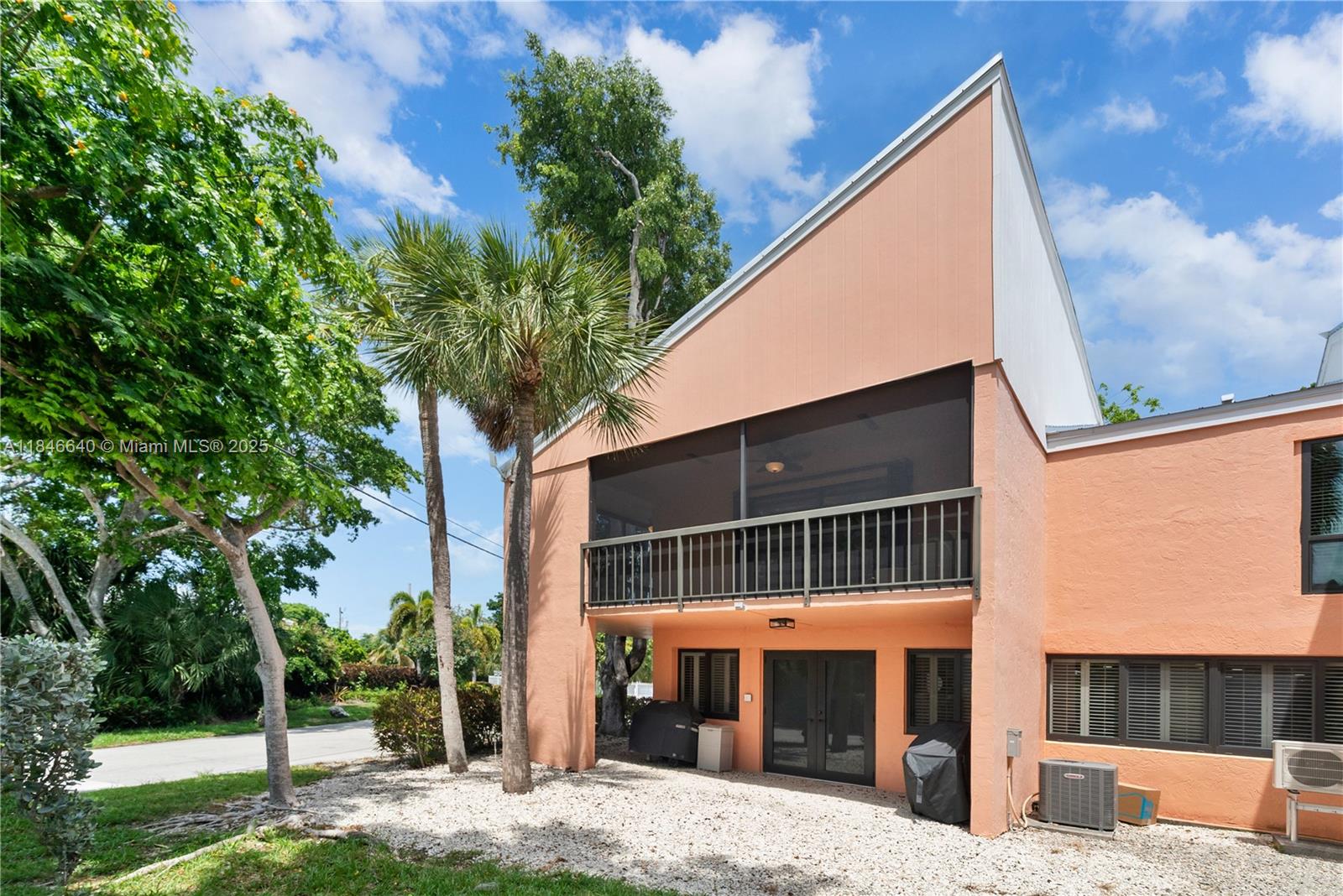 A two-story peach-colored house features a screened-in balcony and a gravel patio area — 9812 Windward Ave, Key Largo FL 33037, KEY LARGO, FL