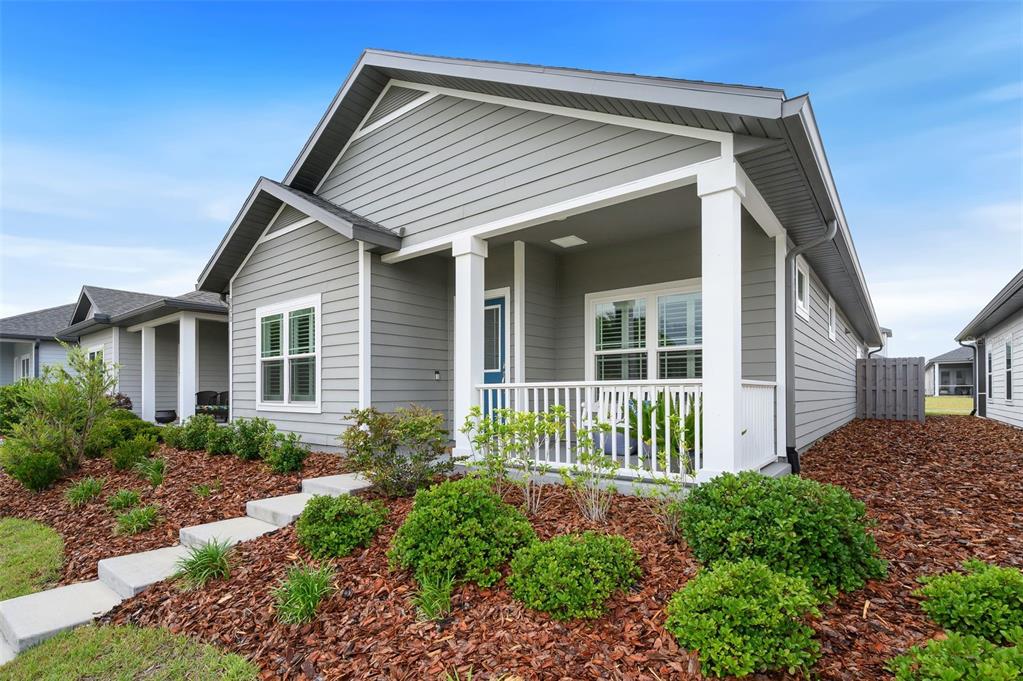 A gray-sided house with a front porch, white railings, and a landscaped yard — 9670 SW 68TH LANE, GAINESVILLE, FL