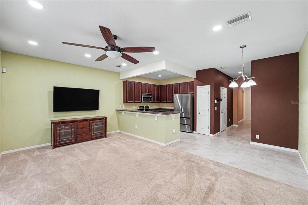 An open-concept living room with carpeted floors connects to a kitchen featuring dark wood cabinets — 6938 46TH WAY N, PINELLAS PARK, FL