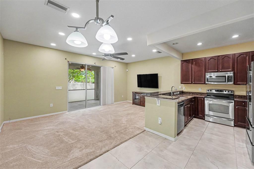 An open-concept living room with carpeted floors connects to a kitchen featuring dark wood cabinets — 6938 46TH WAY N, PINELLAS PARK, FL