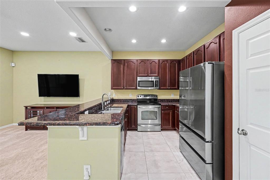 A kitchen with dark wood cabinets, granite countertops, and stainless steel appliances overlooks a living area — 6938 46TH WAY N, PINELLAS PARK, FL