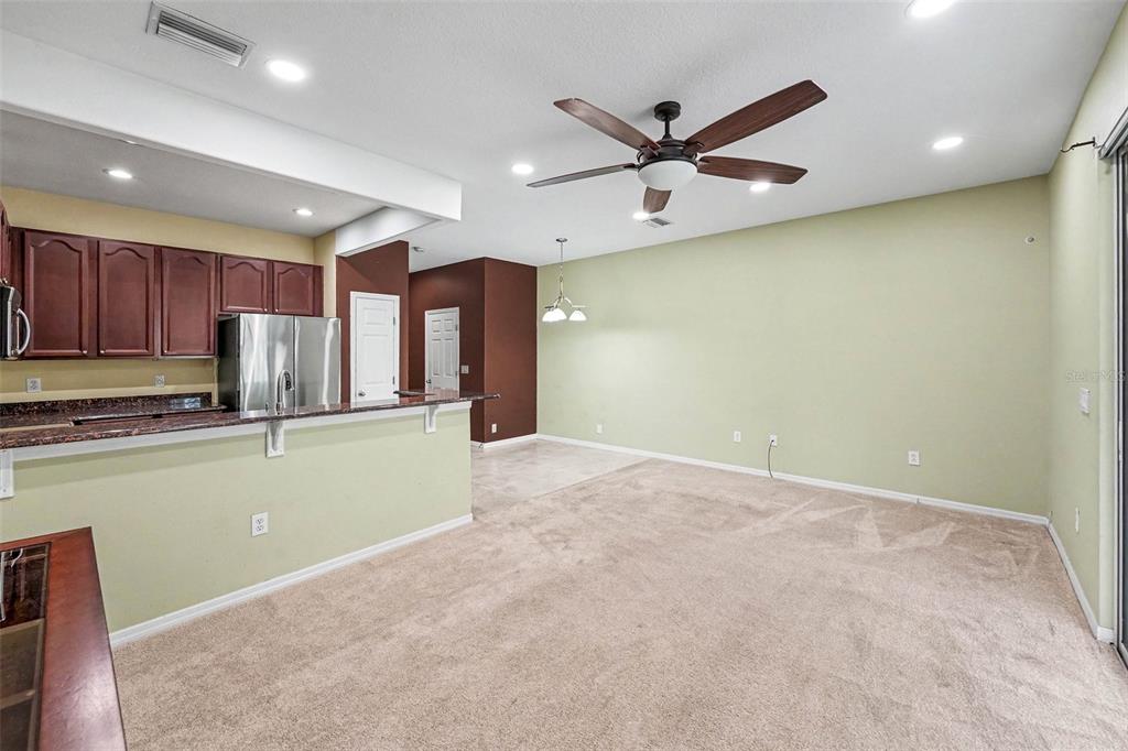 An open-concept living area features beige carpet, a kitchen with dark cabinets, and a ceiling fan — 6938 46TH WAY N, PINELLAS PARK, FL