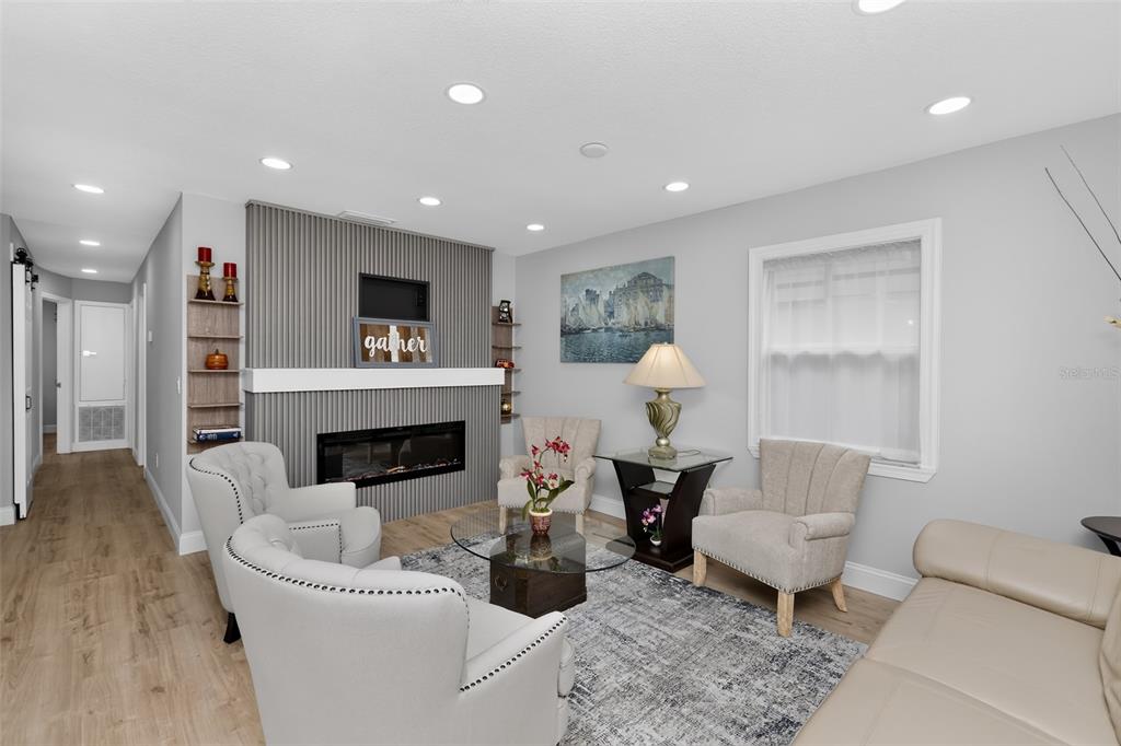 A living room features a gray slatted fireplace wall, light wood flooring, and neutral furniture — 5124 CHILKOOT STREET, TAMPA, FL
