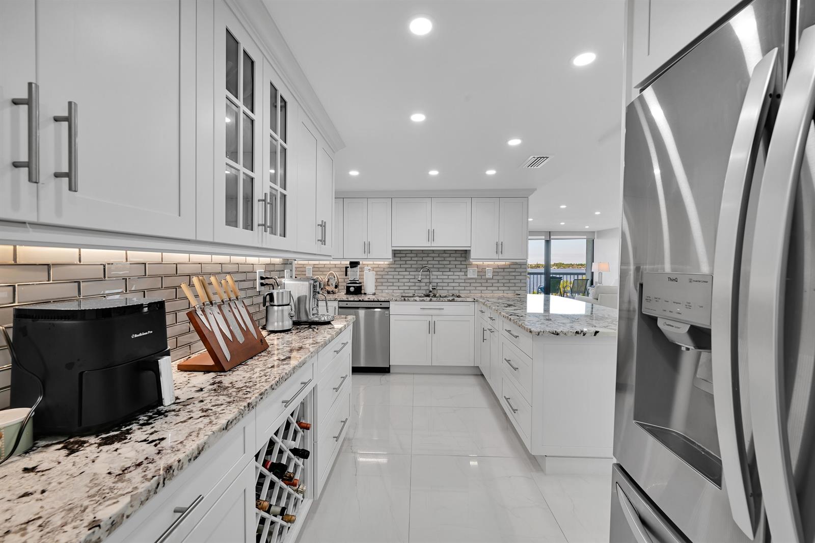 A modern white kitchen features granite countertops, stainless steel appliances, and a wine rack — 3300 S Ocean Boulevard # 306n, Palm Beach FL 33480, PALM BEACH, FL