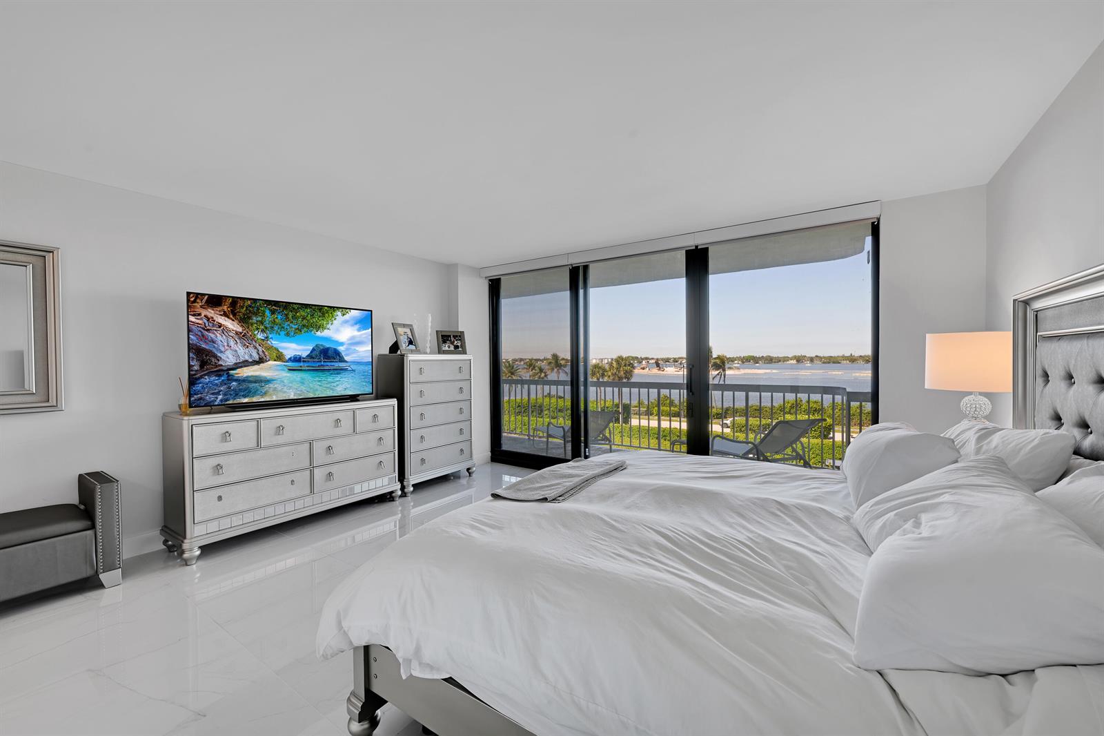 A bedroom features a bed, dresser, television, and floor-to-ceiling windows overlooking a waterfront balcony — 3300 S Ocean Boulevard # 306n, Palm Beach FL 33480, PALM BEACH, FL