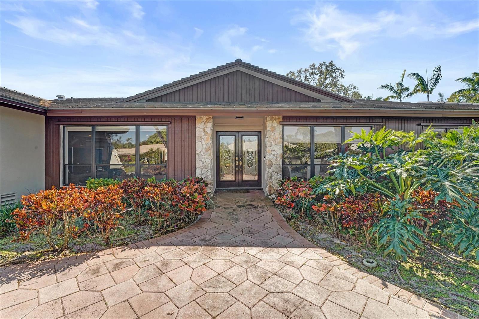 A stone-accented entryway with double glass doors leads to a house with brown wood siding — 9600 Conch Shell Manor, Plantation FL 33324, PLANTATION, FL