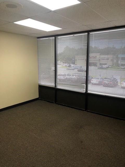 An empty office with beige walls, brown carpet, and large windows covered by horizontal blinds — 7211 N DALE MABRY HIGHWAY N, TAMPA, FL