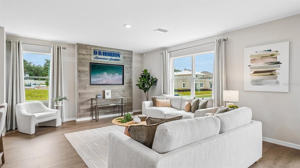 A living room features light wood flooring, a wood-paneled accent wall, and neutral-toned furniture — 17972 ACORN DROP ROAD, LAND O LAKES, FL