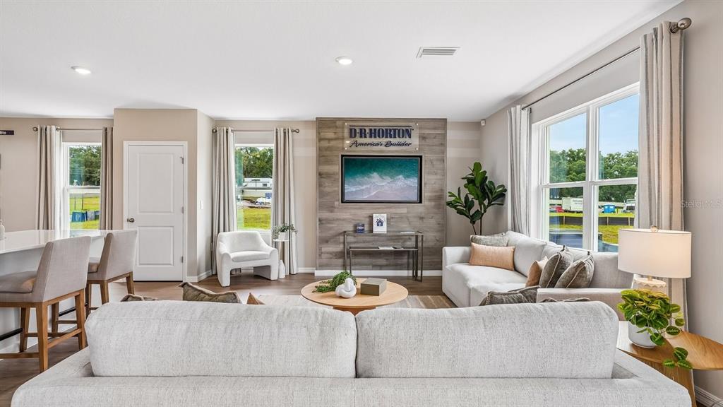 A living room features a wood-paneled accent wall, a sectional sofa, and large windows — 17972 ACORN DROP ROAD, LAND O LAKES, FL