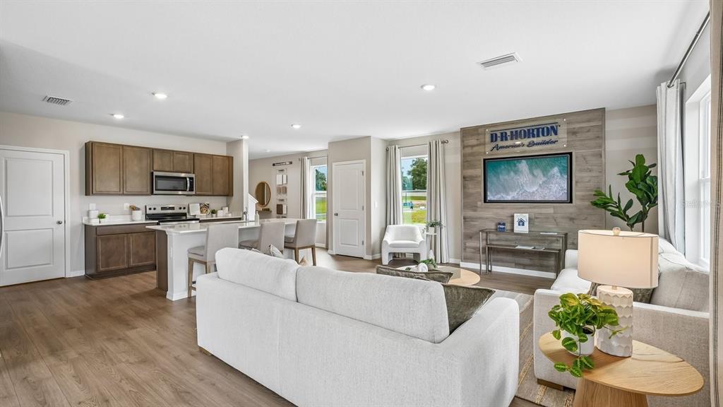 An open-concept living room and kitchen featuring wood-look flooring, light-colored furniture, and a wood-paneled wall — 17972 ACORN DROP ROAD, LAND O LAKES, FL