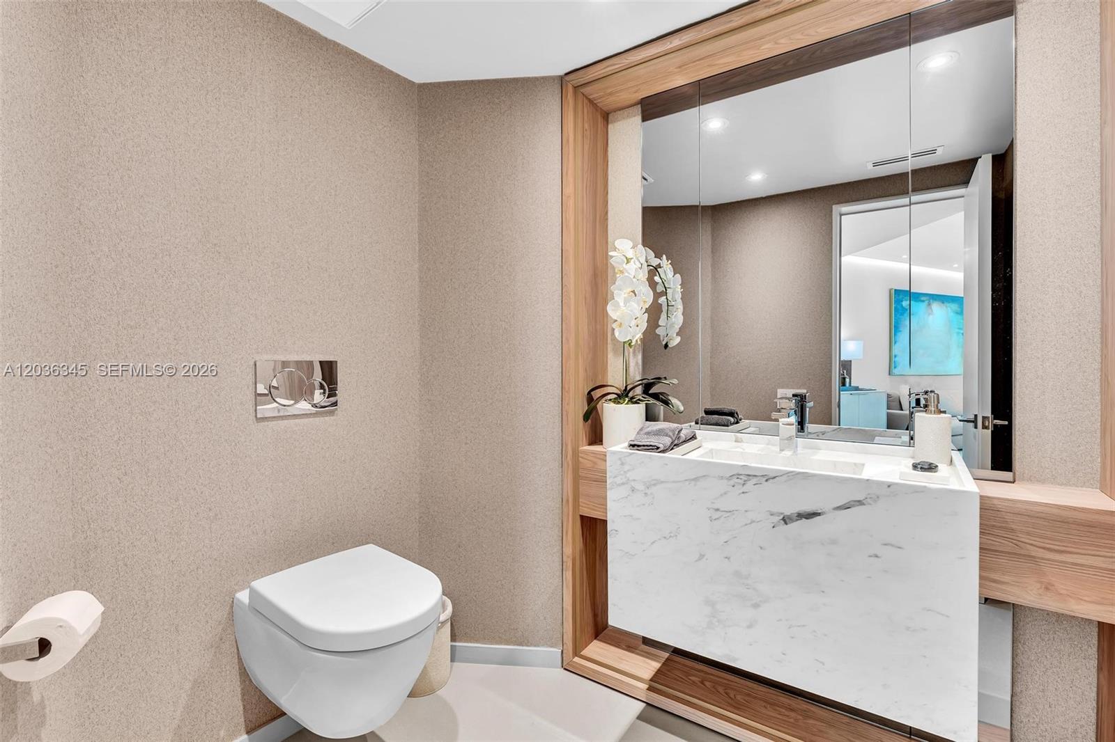 A modern powder room features a wall-mounted toilet, marble vanity, and wood-framed mirror — 2127 Brickell Ave # 1002, Miami FL 33129, MIAMI, FL