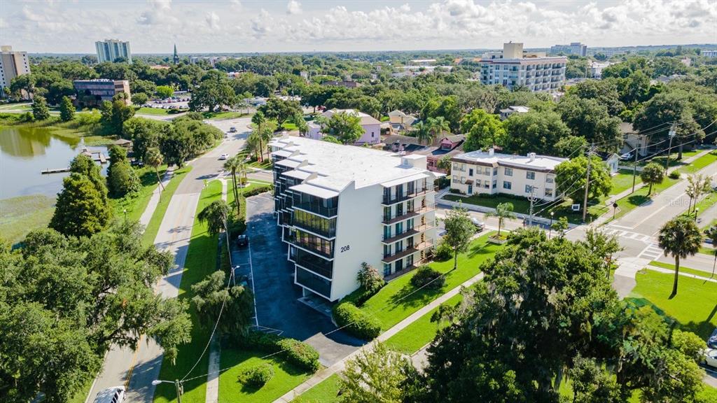 An aerial view shows a multi-story apartment building with balconies next to a lake — 208 LAKE HOWARD DRIVE NW UNIT 104, WINTER HAVEN, FL