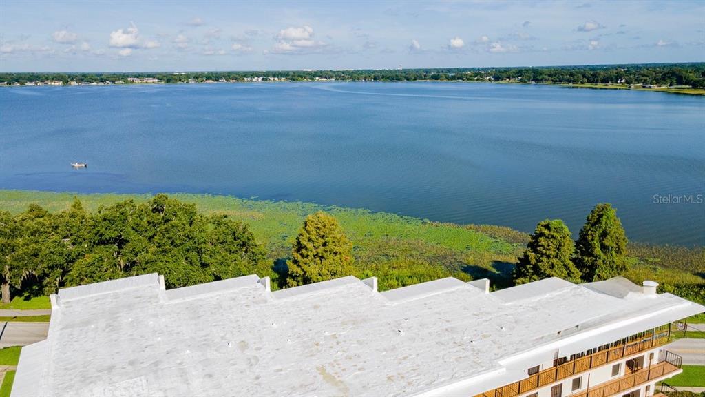 An aerial view shows a flat-roofed building overlooking a large lake with vegetation — 208 LAKE HOWARD DRIVE NW UNIT 104, WINTER HAVEN, FL