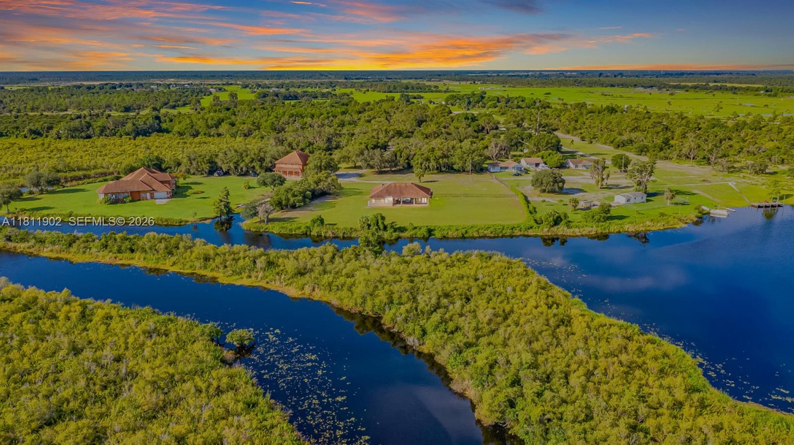 An aerial view shows several houses situated on a grassy lot beside a winding river — 37511 Washington Loop Road, Punta Gorda FL 33982, PUNTA GORDA, FL