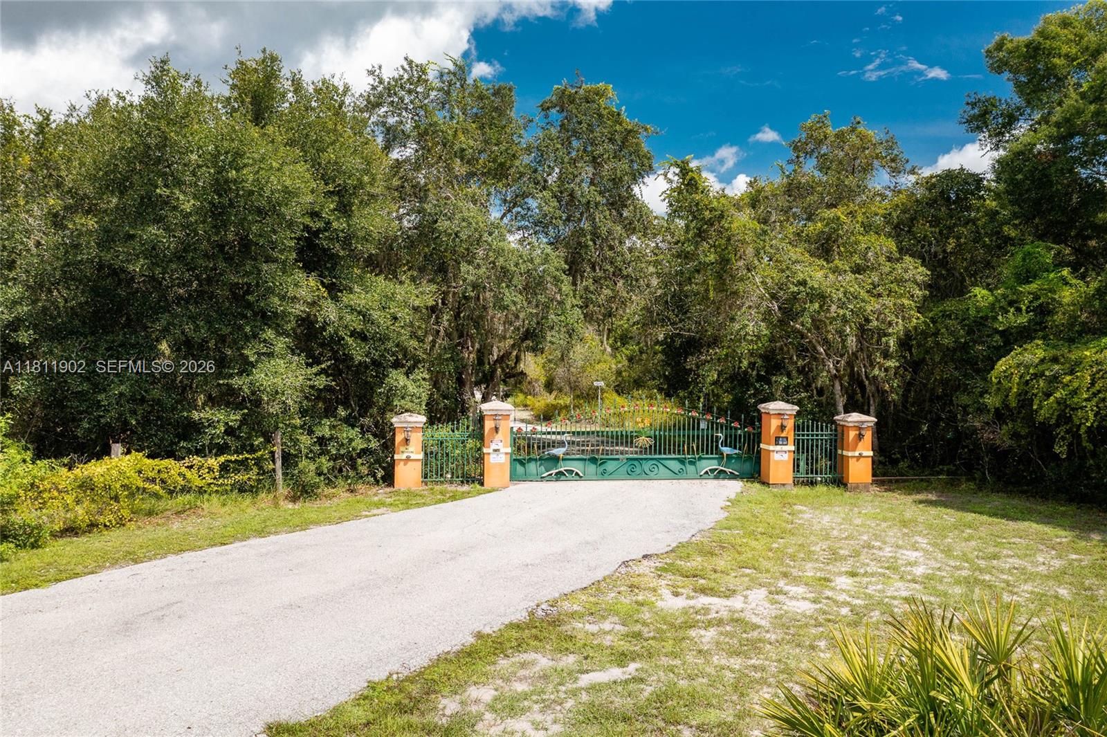 A paved driveway leads to a green metal gate flanked by four orange stucco pillars — 37511 Washington Loop Road, Punta Gorda FL 33982, PUNTA GORDA, FL