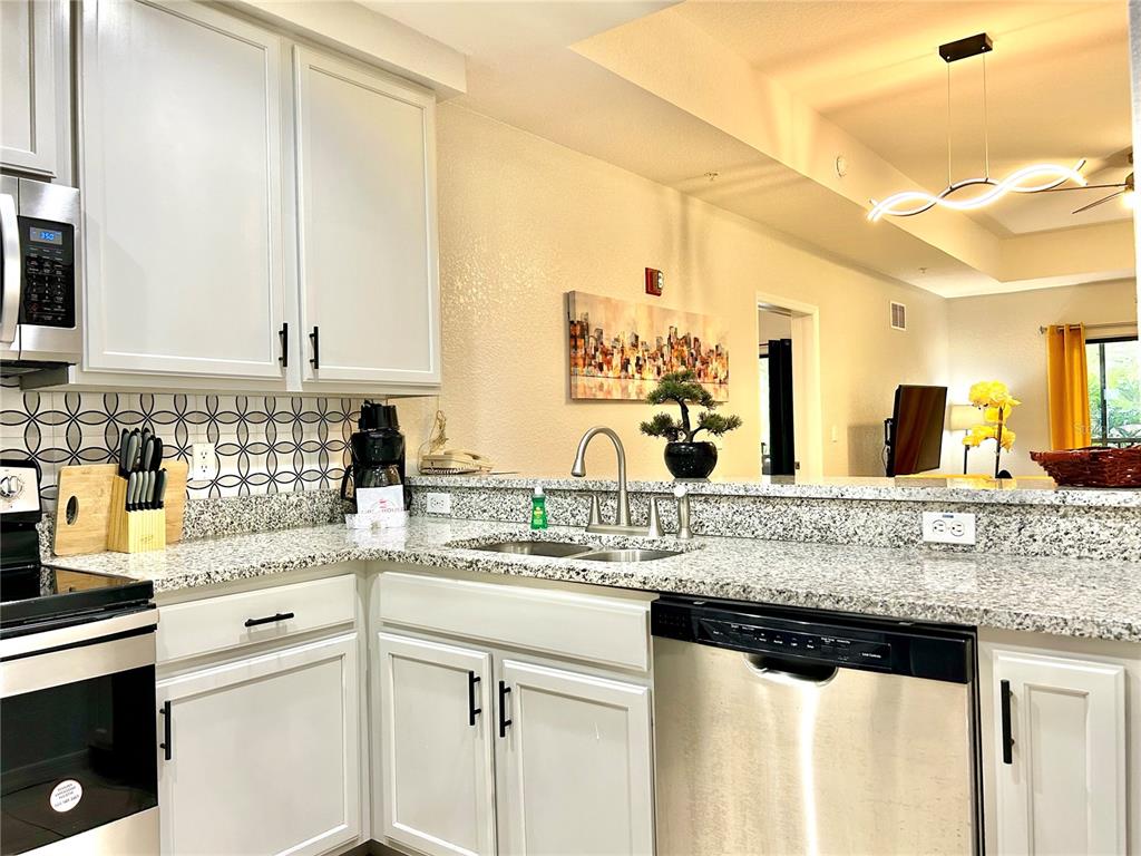 A kitchen features white cabinets, granite countertops, a patterned backsplash, and stainless steel appliances — 9055 TREASURE TROVE LANE UNIT 105, KISSIMMEE, FL