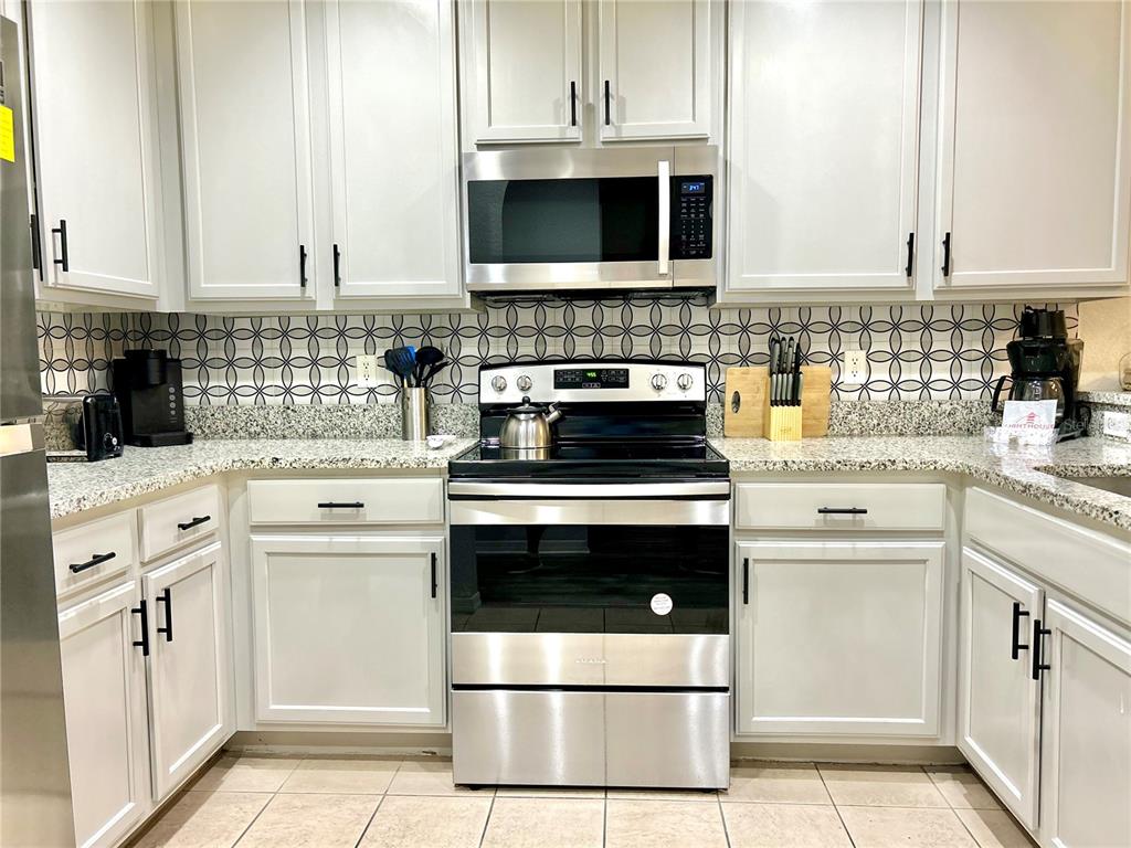 A kitchen features white cabinets, stainless steel appliances, granite countertops, and a patterned tile backsplash — 9055 TREASURE TROVE LANE UNIT 105, KISSIMMEE, FL