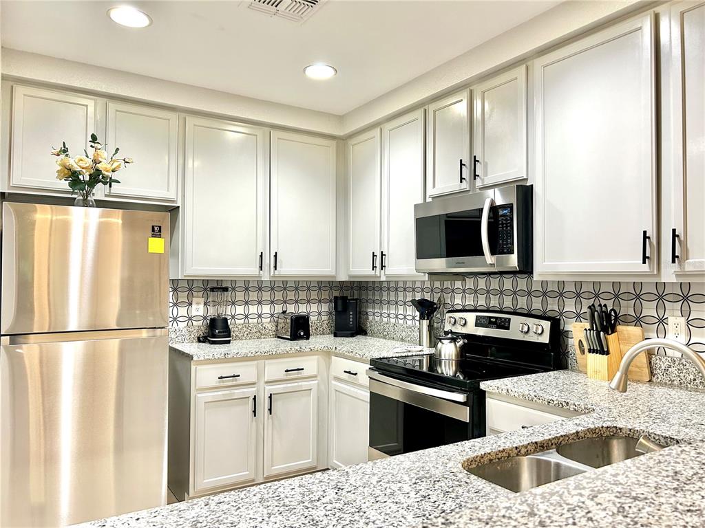 A kitchen features white cabinets, stainless steel appliances, granite countertops, and a patterned tile backsplash — 9055 TREASURE TROVE LANE UNIT 105, KISSIMMEE, FL