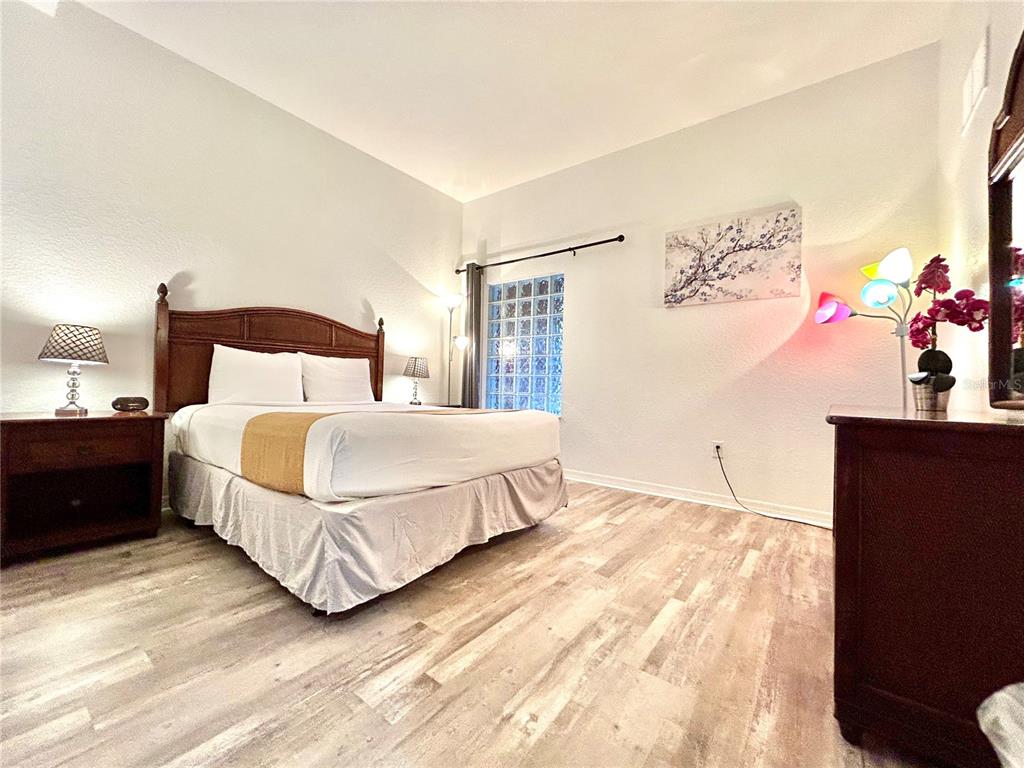 A bedroom features a bed with a wooden headboard, light wood-look flooring, and glass blocks — 9055 TREASURE TROVE LANE UNIT 105, KISSIMMEE, FL