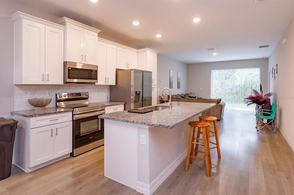 A kitchen with white cabinets, stainless steel appliances, and a granite-topped island with stools — 884 KLONDIKE STREET, WINTER GARDEN, FL
