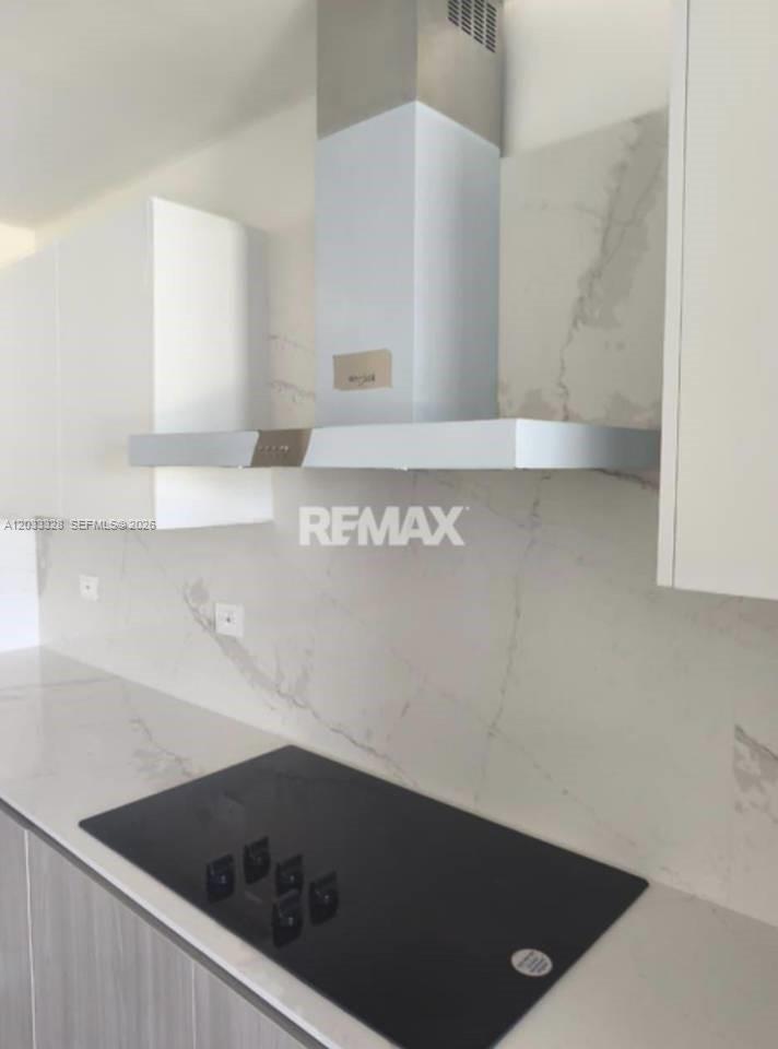 A modern kitchen features a black induction cooktop, white cabinets, and a marble-patterned backsplash — 1 Cap Cana # 1, FL, FL