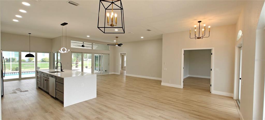 An open-concept kitchen and living area features light wood flooring, a large island, and chandeliers — 2531 PEBBLE CREEK PLACE, PORT CHARLOTTE, FL