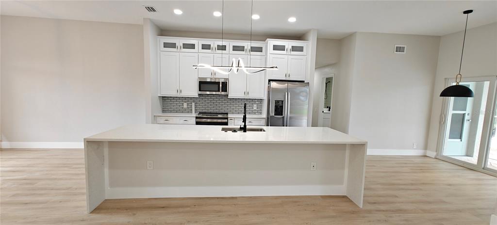 A modern kitchen features white cabinetry, a large quartz island, and light wood-look flooring — 2531 PEBBLE CREEK PLACE, PORT CHARLOTTE, FL