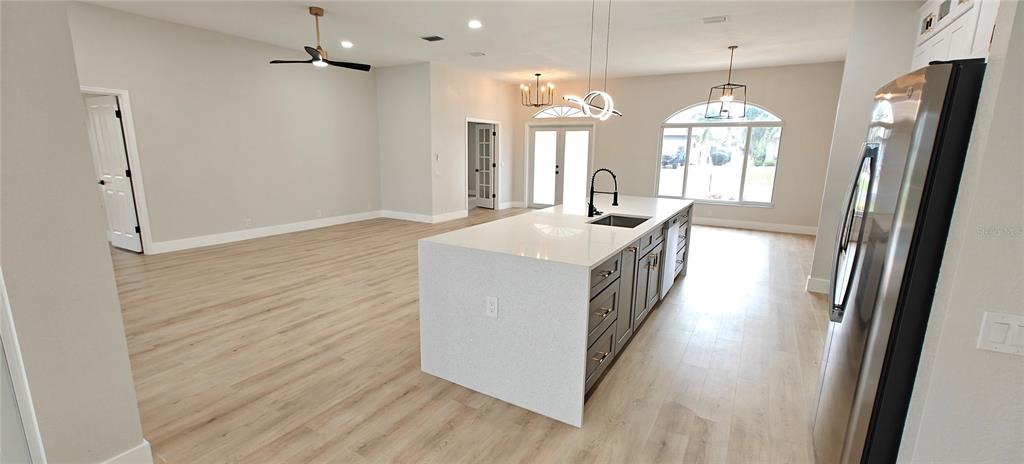 A modern kitchen with a white quartz island and stainless steel appliances opens to a living area — 2531 PEBBLE CREEK PLACE, PORT CHARLOTTE, FL