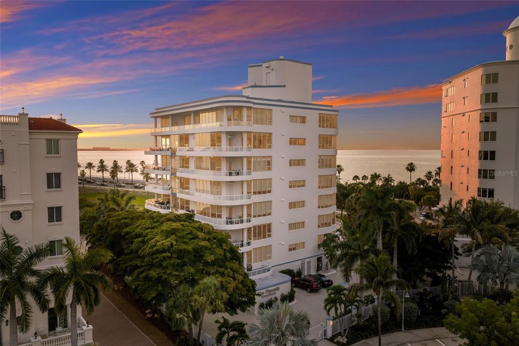 An aerial view of a multi-story white residential building located near the ocean at sunset — 136 GOLDEN GATE POINT UNIT 602, SARASOTA, FL