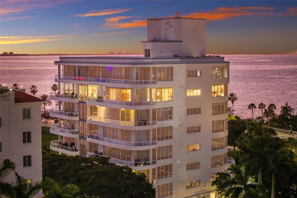 An exterior view of a multi-story white apartment building overlooking the ocean at sunset — 136 GOLDEN GATE POINT UNIT 602, SARASOTA, FL
