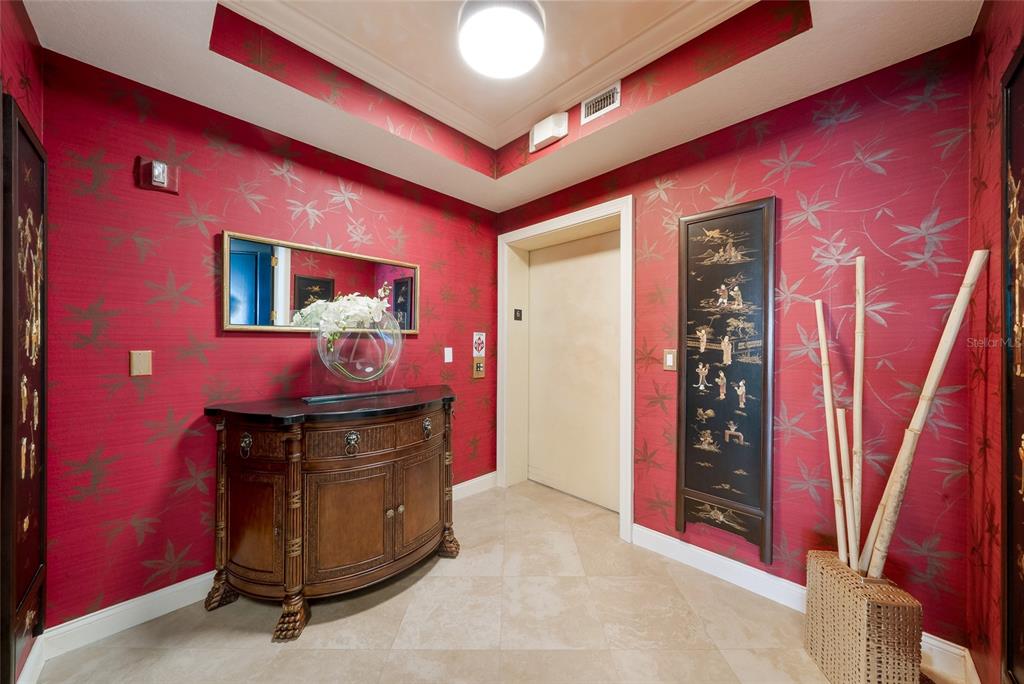A foyer with red patterned wallpaper, a wooden console table, and an elevator door — 136 GOLDEN GATE POINT UNIT 602, SARASOTA, FL