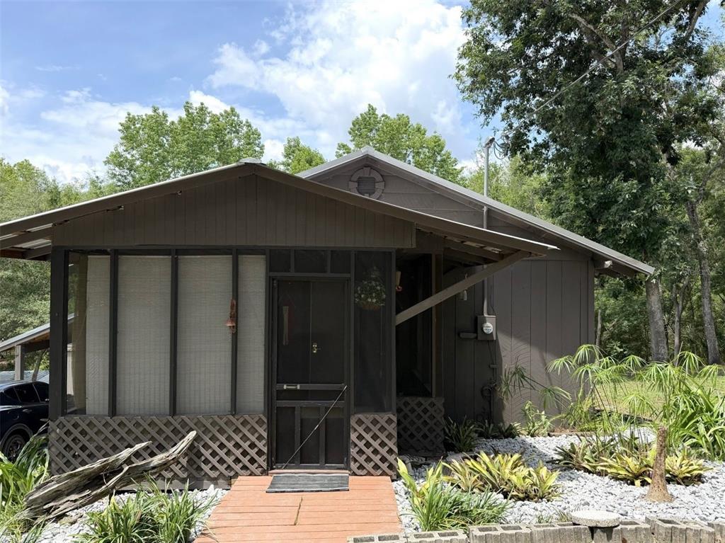 A brown, single-story house features a screened-in porch, a wooden walkway, and gravel landscaping — 18930 NE 143RD AVENUE, FORT MC COY, FL