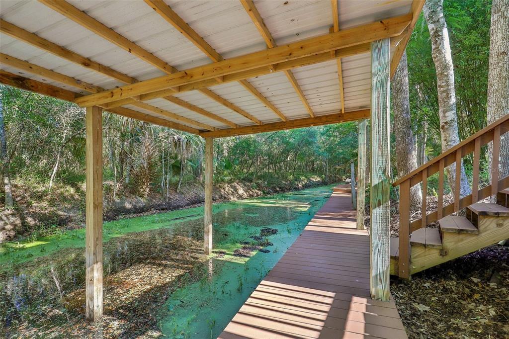 A wooden deck with a covered boat slip overlooks a green, algae-covered canal — 18930 NE 143RD AVENUE, FORT MC COY, FL