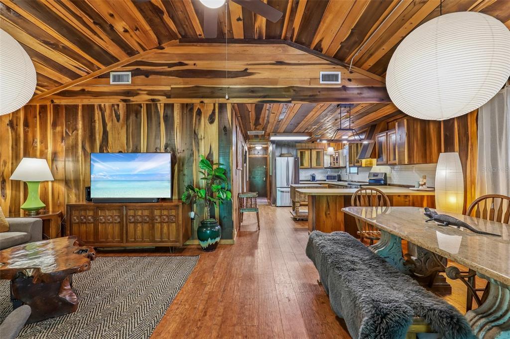 An open-concept living and dining area features wood-paneled walls, vaulted ceilings, and rustic furniture — 18930 NE 143RD AVENUE, FORT MC COY, FL