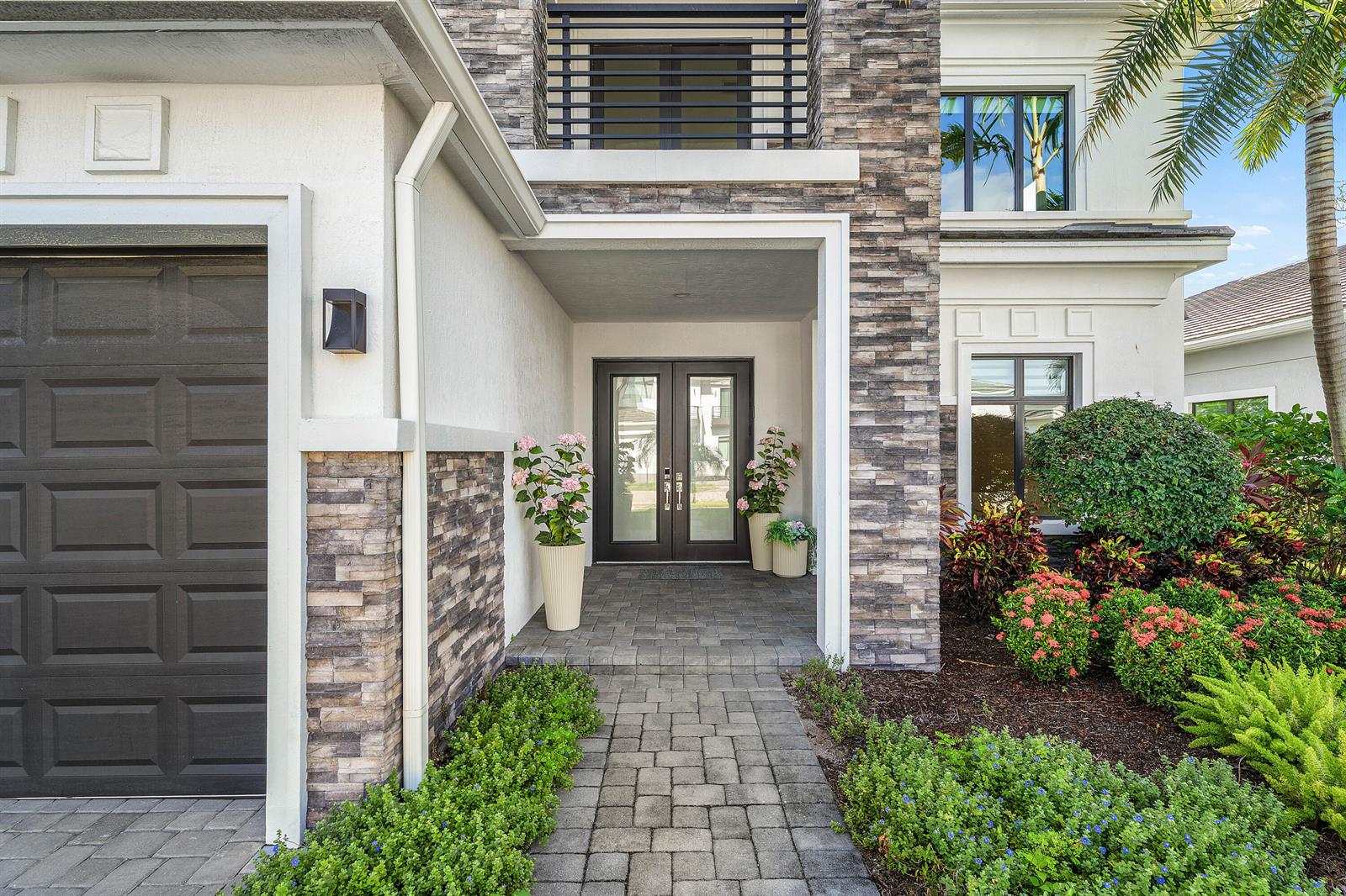 The exterior of a modern home features a stone facade, double front doors, and landscaping — 7409 NW 25th Terrace, Boca Raton FL 33496, BOCA RATON, FL