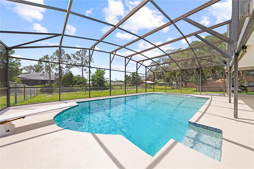 A swimming pool with a diving board is enclosed by a screened lanai in a backyard — 6570 BAY SHORE DRIVE, ST CLOUD, FL
