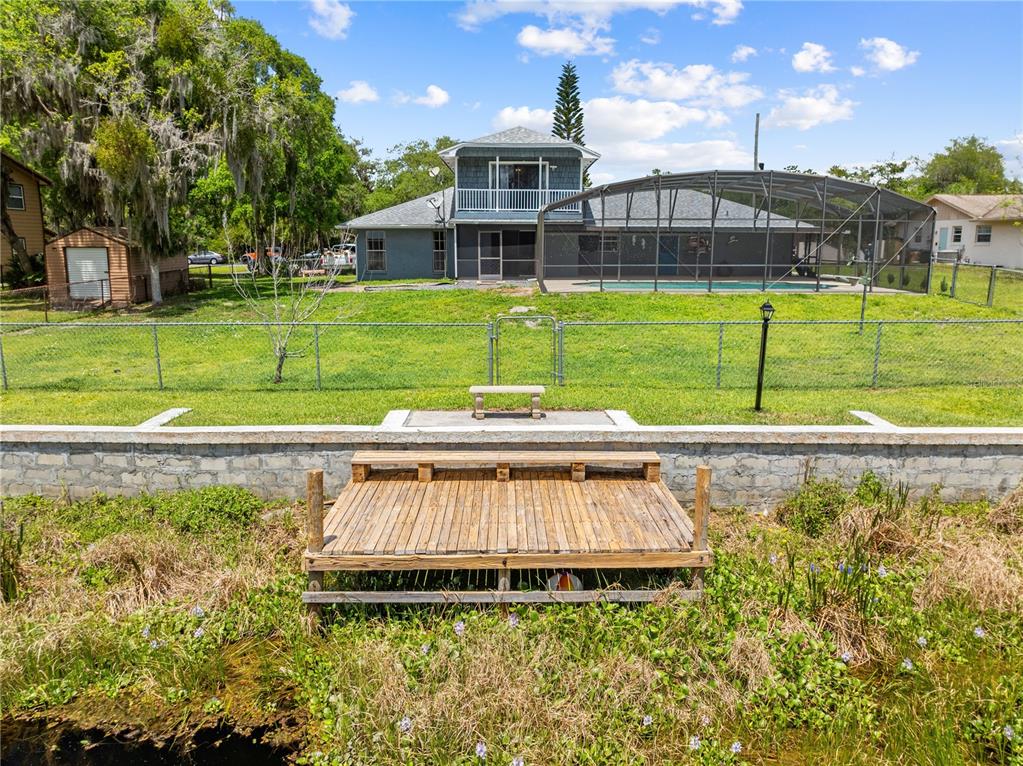 A wooden dock sits in front of a fenced backyard with a pool enclosure — 6570 BAY SHORE DRIVE, ST CLOUD, FL