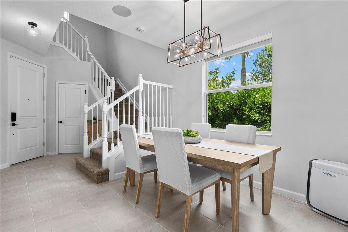 A dining area features a wooden table, modern chandelier, and a staircase with white railings — 16493 Helix Court, Westlake FL 33470, WESTLAKE, FL