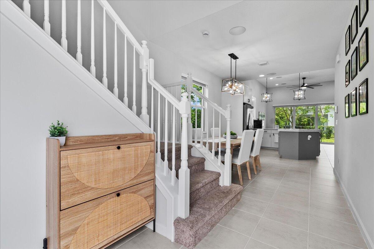 A staircase with a wooden shoe cabinet sits beside an open-concept kitchen and dining area — 16493 Helix Court, Westlake FL 33470, WESTLAKE, FL