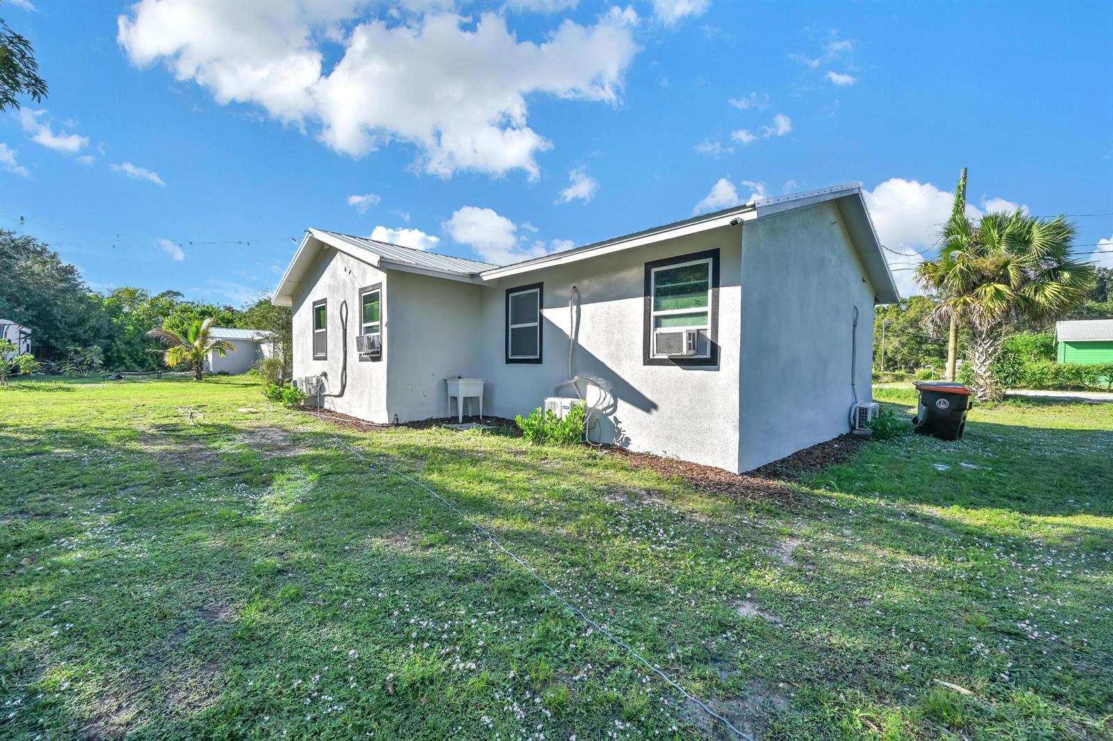 The exterior of a light-colored, single-story house features a metal roof and window air conditioners — 6385 86th Place, Vero Beach FL 32958, VERO BEACH, FL