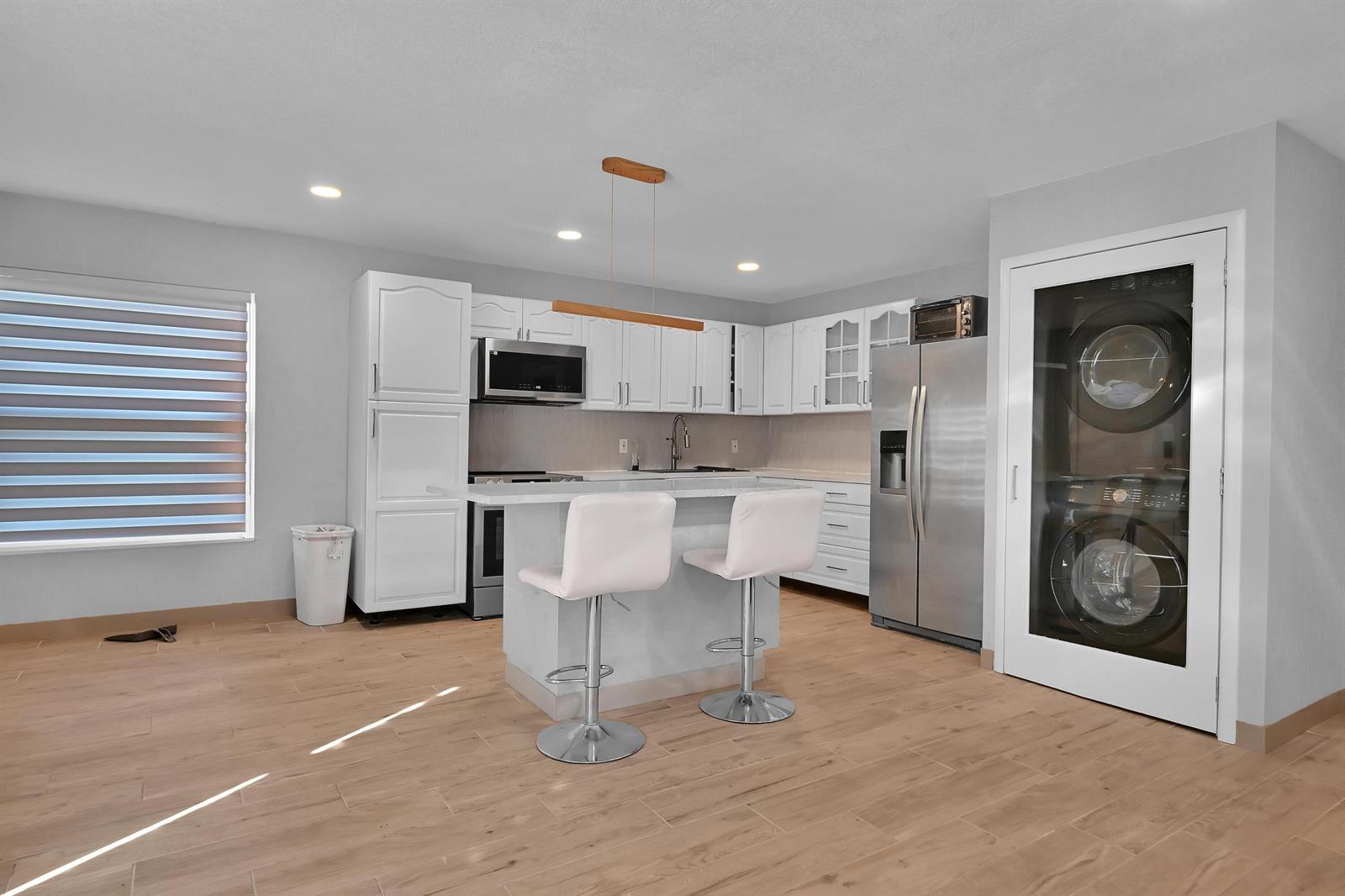 A kitchen features white cabinets, stainless steel appliances, a central island, and a stacked laundry unit — 6385 86th Place, Vero Beach FL 32958, VERO BEACH, FL