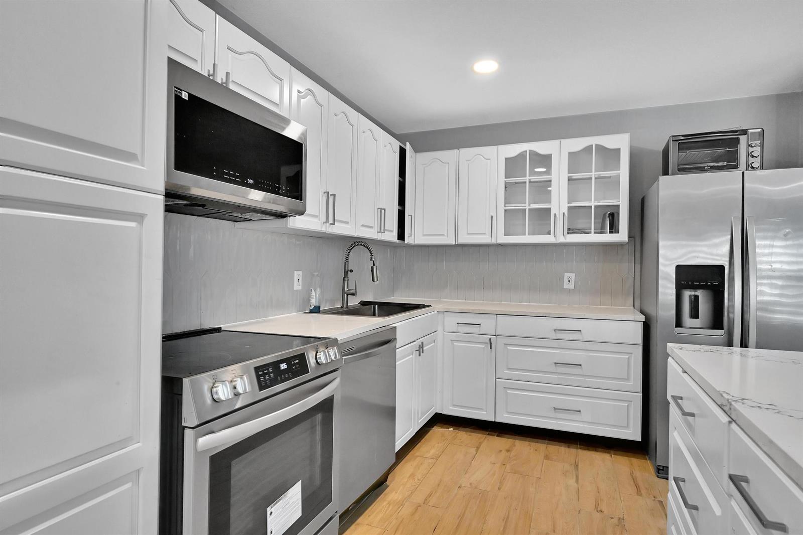 A kitchen with white cabinets, stainless steel appliances, a tiled backsplash, and light wood flooring — 6385 86th Place, Vero Beach FL 32958, VERO BEACH, FL