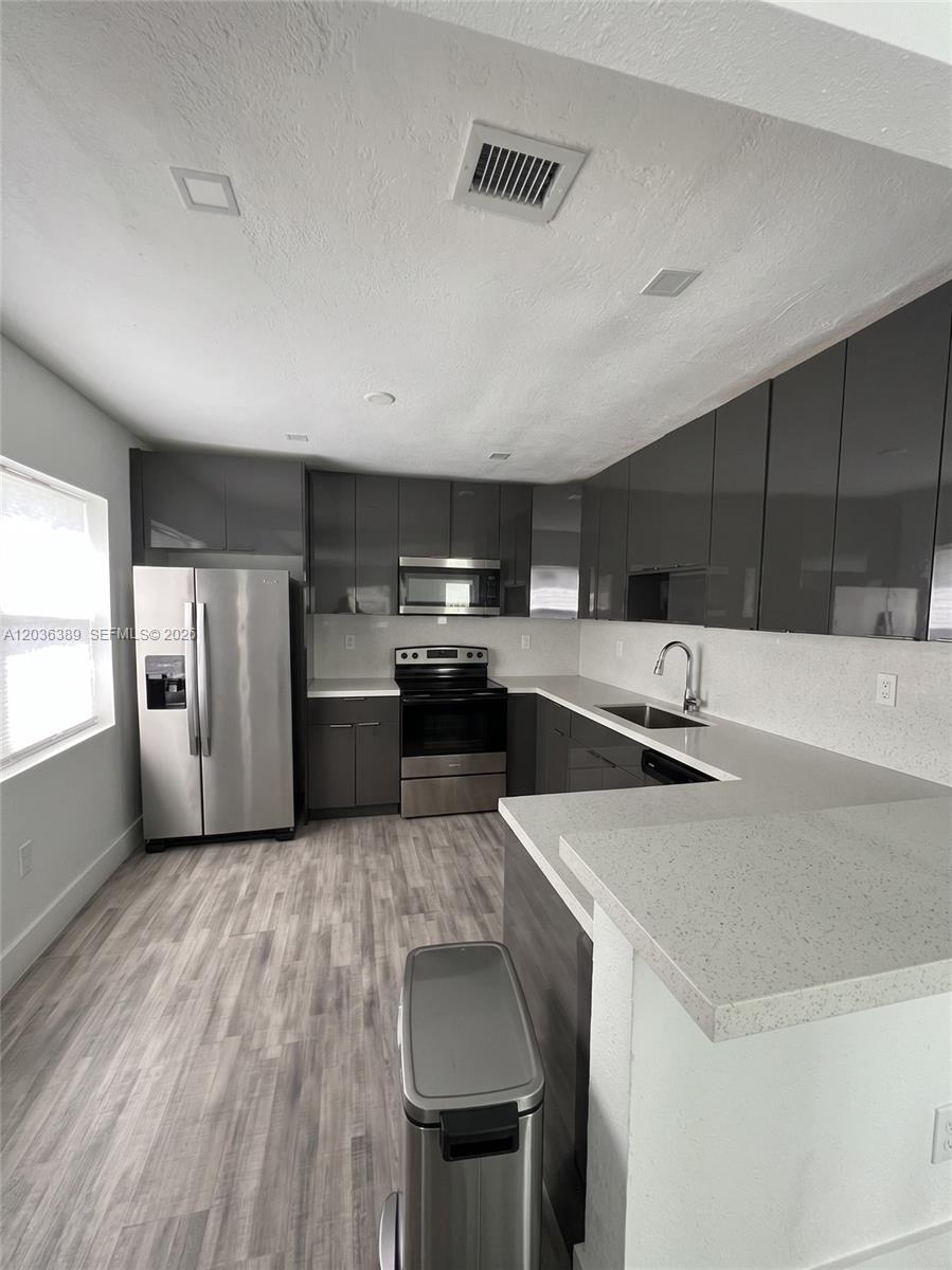 A modern kitchen features gray high-gloss cabinets, stainless steel appliances, and light-colored quartz countertops — 2847 Polk St # 1, Hollywood FL 33020, HOLLYWOOD, FL