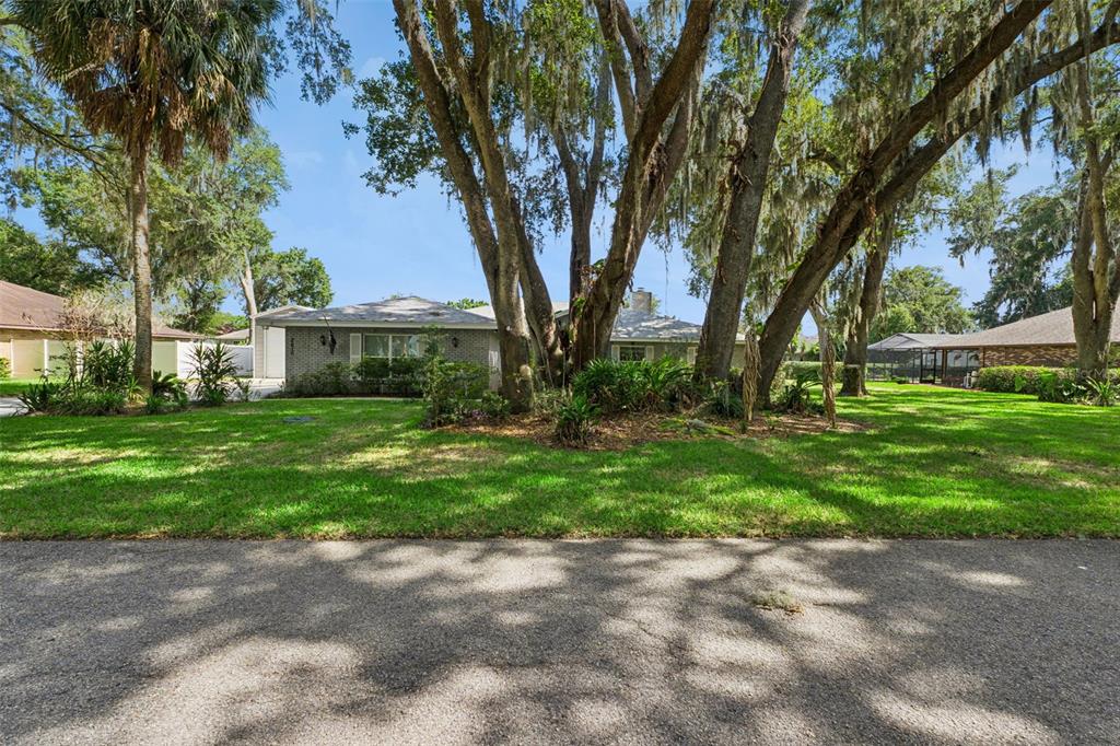 A single-story brick house sits behind large trees with Spanish moss on a grassy lot — 2610 TWELVE POINT DRIVE, LAKELAND, FL
