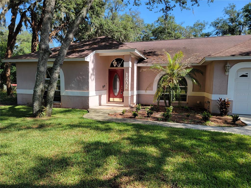 A single-story house with a pink stucco exterior, arched windows, and a red front door — 1602 YEOMANS PATH, LAKELAND, FL