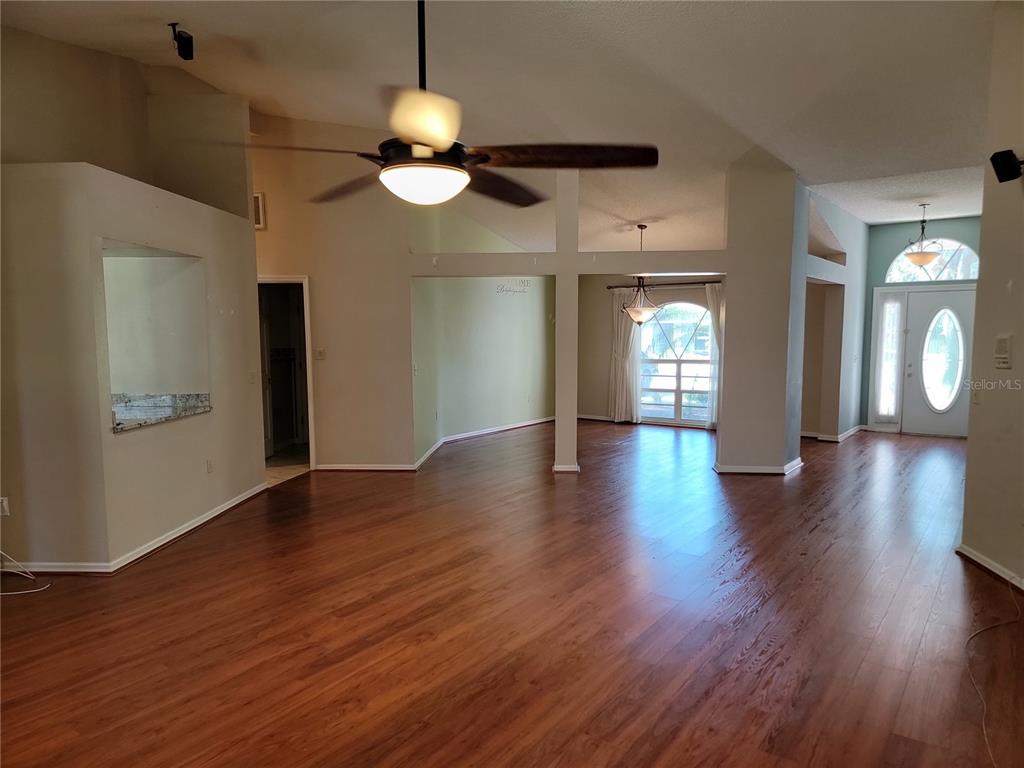 An open-concept living area features wood-look flooring, vaulted ceilings, and a ceiling fan — 1602 YEOMANS PATH, LAKELAND, FL