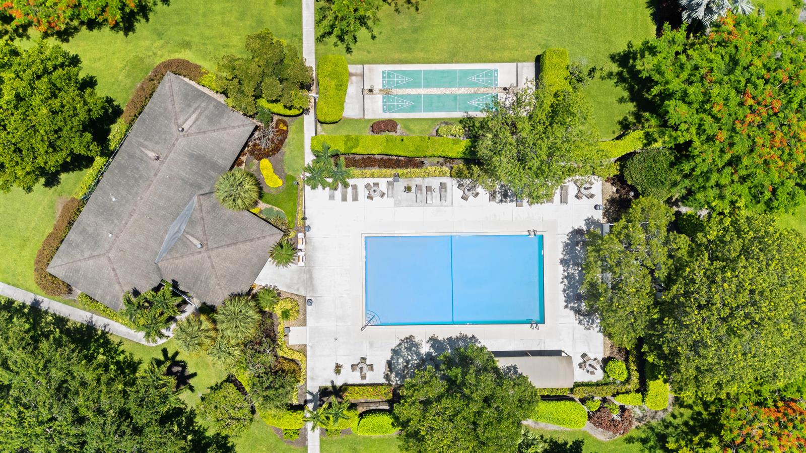 An aerial view shows a swimming pool, shuffleboard courts, and a building surrounded by trees — 3510 Oaks Way # 406, Pompano Beach FL 33069, POMPANO BEACH, FL