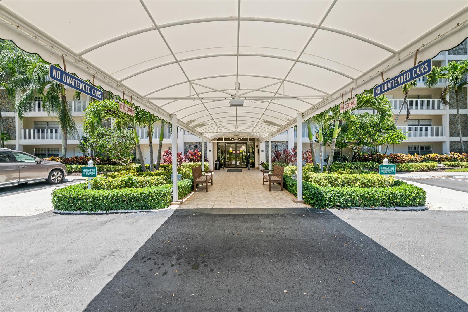 A covered entrance walkway leads to a building entrance with benches and tropical landscaping — 3510 Oaks Way # 406, Pompano Beach FL 33069, POMPANO BEACH, FL
