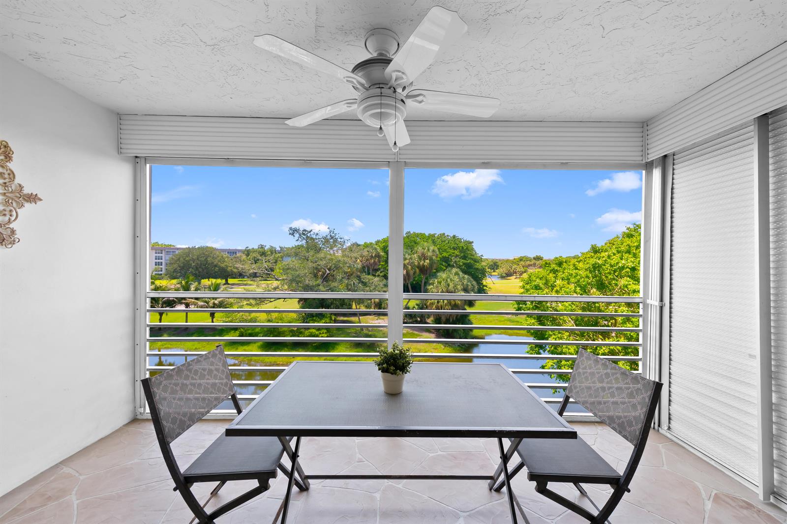 A screened-in balcony features a table with two chairs, a ceiling fan, and a golf course view — 3510 Oaks Way # 406, Pompano Beach FL 33069, POMPANO BEACH, FL