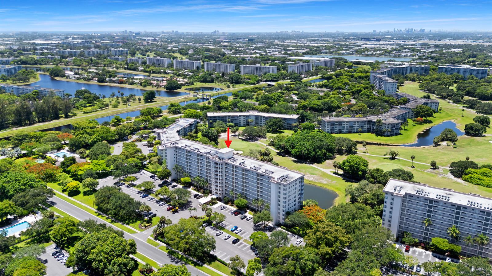 An aerial view shows a multi-story apartment building surrounded by green spaces, parking lots, and lakes — 3510 Oaks Way # 406, Pompano Beach FL 33069, POMPANO BEACH, FL